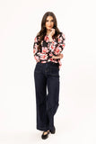 Woman wearing a floral blouse and dark jeans on a white background Seeking Lola Connected Blouse - Bold Rosette