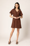 A woman modeling a brown short-sleeve mini dress with a V-neckline and scalloped hem, paired with brown wedge sandals, against a plain light beige studio background. Seeking Lola Scallop Shortie Dress - Chestnut