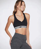 A woman wearing a black sports bra with the Skechers logo on the elasticized hem and matching gray activewear pants.