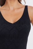 Close-up of a woman wearing a black sleeveless V-neck top with a subtle geometric textured pattern, set against a plain light background.