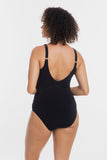 A woman shown from the back wearing a black one-piece swimsuit with thin shoulder straps and a deep V-shaped back cutout, photographed against a plain light gray studio background.