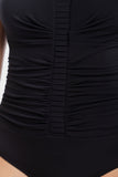 Close-up of a black one-piece swimsuit or bodysuit with ruched vertical detailing down the center and gathered fabric on both sides.