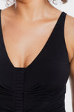 Close-up of a model wearing a black sleeveless top with a deep V-neckline and gathered pleated detailing at the center bust.