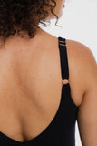 Close-up back view of a person wearing a black ribbed tank top with a wide adjustable shoulder strap featuring a small gold metal ring and a light beige wooden bead accent.