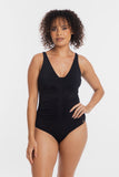 A woman modeling a black one-piece swimsuit with a ruched front and deep V-neckline, photographed against a clean light gray studio background.
