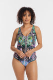 A woman modeling a one-piece swimsuit with a vibrant multicolor print featuring zebra stripes, tropical leaves, and floral patterns in green, blue, pink, and purple on a light gray studio background.