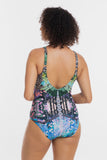 A woman shown from the back wearing a one-piece swimsuit with a colorful abstract and floral print, set against a plain light gray studio background.