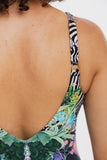 Close-up back view of a person wearing a one-piece swimsuit with a tropical floral print and black-and-white zebra print shoulder strap, against a plain white background.