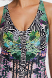 Close-up of a sleeveless V-neck swimsuit or dress with a mixed print combining zebra stripes, tropical leaves, and floral motifs in black, white, green, pink, and blue.