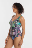 A woman modeling a one-piece swimsuit with a multicolor tropical and zebra print, shown from a side profile against a light gray studio background.