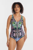 A woman modeling a one-piece swimsuit with a complex multicolor print featuring zebra stripes, green tropical leaves, and pink and purple accents, set against a plain light gray background.