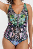 A woman wearing a one-piece swimsuit with a complex multicolor print featuring zebra stripes, tropical leaves, and floral motifs in green, pink, purple, and blue on a black background.