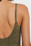 Close-up back view of a person wearing a patterned olive green tank top with thin straps and a small gold ring detail.