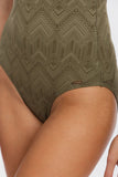 Close-up of a person wearing a high-waisted olive green swimsuit with a geometric pattern, showing the hip and upper thigh area against a light background.