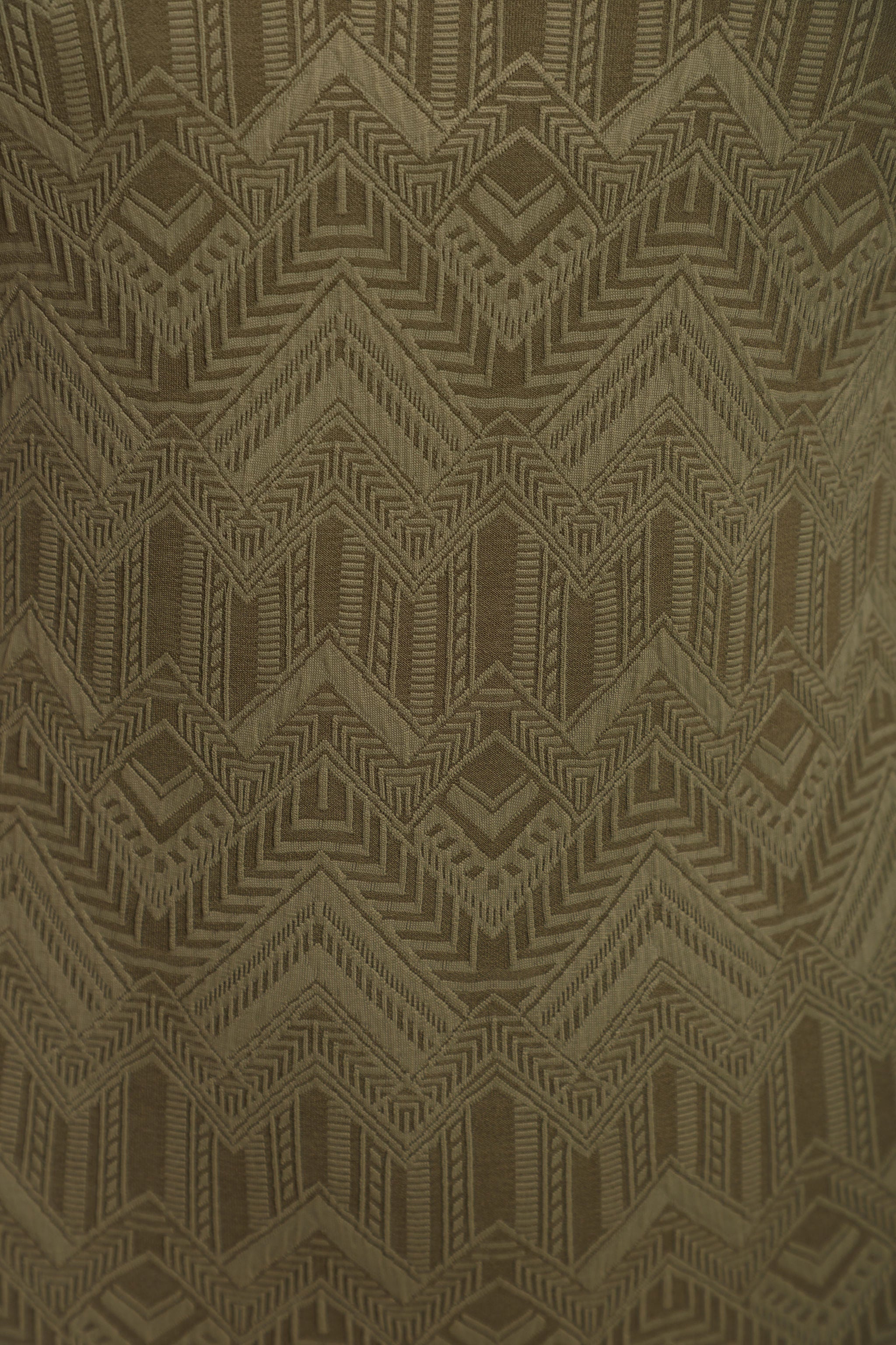 A close-up of a woven fabric with a repeating geometric pattern in olive green and brown.