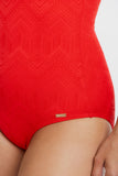 Close-up of a plus-size model wearing a bright red one-piece swimsuit with a subtle geometric pattern and a small gold brand tag near the hip.