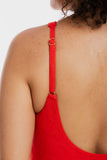 Close-up back view of a person wearing a bright red textured one-piece swimsuit or top, showing the thin adjustable shoulder strap with a small gold-tone ring buckle.