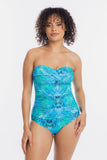 A woman modeling a strapless one-piece swimsuit with a vibrant blue and turquoise abstract pattern against a plain white background.