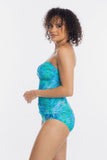 A woman modeling a strapless one-piece swimsuit with a blue and green marbled pattern, photographed against a plain white studio background.