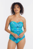 A woman modeling a strapless one-piece swimsuit with a vibrant blue and green tropical leaf pattern against a plain white studio background.