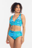 A woman modeling a two-piece bikini swimsuit with a vibrant blue and green tropical floral print against a plain white background.