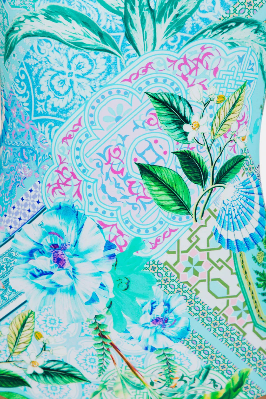 A close-up of a vibrant, multicolored patterned fabric featuring tropical floral motifs, green leaves, and intricate geometric and paisley designs in shades of turquoise, pink, green, and white. TOGS Peru Lucca Reversible Square One Piece