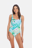 A woman modeling a one-piece swimsuit with a colorful tropical and floral pattern in shades of blue, green, and white, set against a plain light gray studio background. TOGS Peru Lucca Reversible Square One Piece