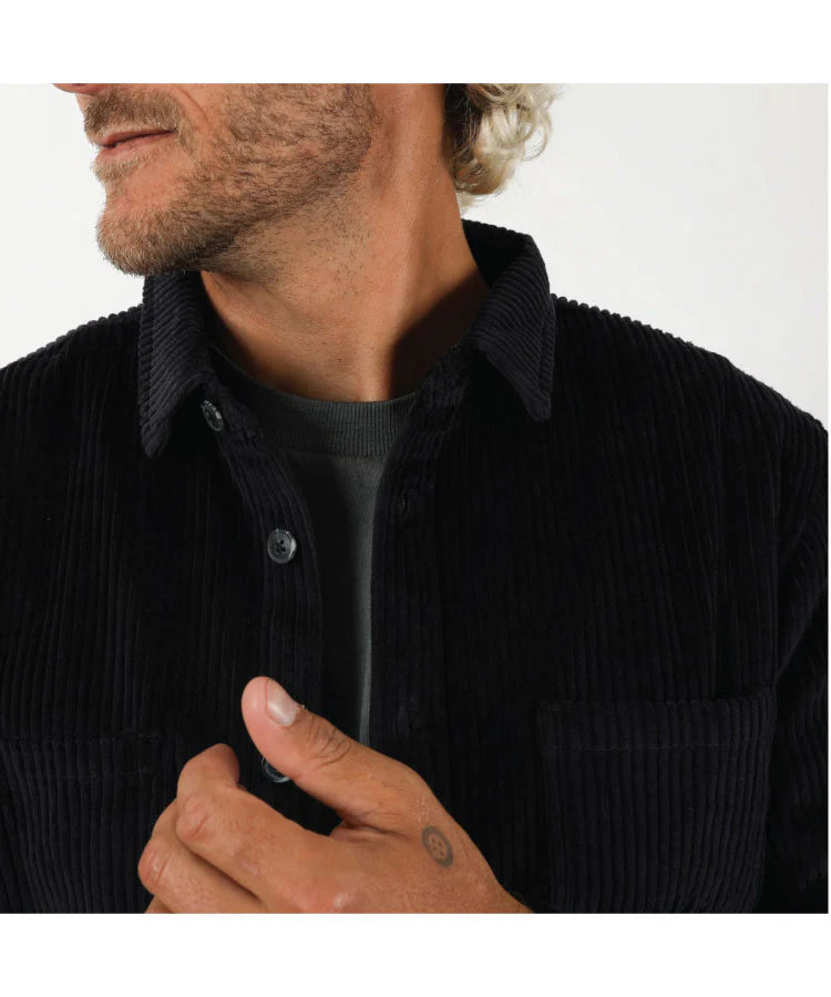 Close-up of a person wearing a black corduroy shirt with a plain background T&C Motion LS Cord Shirt - Midnight