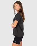 Woman wearing a black t-shirt and shorts with visible branding on a light gray background