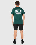 A man viewed from the back wearing a dark green t-shirt with a large white graphic on the back that reads 'UNIT', paired with black shorts, socks, and shoes, set against a solid light gray background. Unit Mens Tees - Index - Forest Green