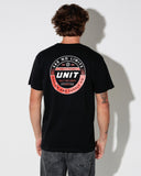 A man viewed from behind wearing a black t-shirt with a large circular graphic on the back in red, white, and black. The graphic features the text 'SEE NO LIMITS', 'UNIT', and 'BUILT FOR LEGACY' from the brand 'Design and Supply Co'.