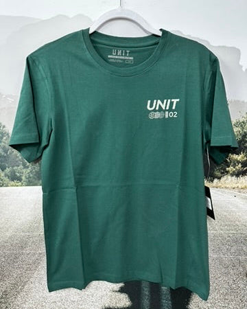 Green t-shirt with 'UNIT' logo on a hanger against a blurred outdoor background