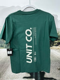 Green t-shirt with 'UNIT CO.' branding on a hanger against a blurred outdoor background.