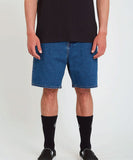 A person wearing a black T-shirt and blue denim shorts, with socks and shoes, standing against a white background. Volcom Billow Denim Shorts - Oliver Mid Blue
