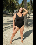 Woman in a black swimsuit standing on a sandy beach with palm trees in the background