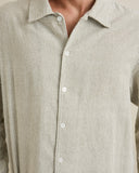 Close-up of a person wearing a long-sleeve button-up shirt with fine vertical stripes in beige and dark brown or black, featuring white buttons. Rhythm Men's Bank Stripe LS Shirt – Olive