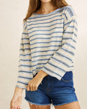 A woman wearing a cream and blue striped long-sleeve top with frayed edges, paired with blue denim shorts, against a plain beige background.