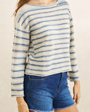 A woman wearing a long-sleeve knit top with horizontal cream, light blue, and navy stripes, paired with blue denim shorts against a plain beige background.