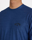 Billabong Mens Shoreline UPF 50 Long Sleeve Rashguard in Denim Heather blue close up view highlighting the premium silk touch quick dry fabric weave texture double stitched lower hemline and detailed brand graphic finish, sold by Point Break Cambridge local family surf shop at 63 Duke street.