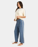 Woman wearing a cream top and blue Billabong pants with a white stripe down the hem. Button fasten, front pockets and belt loops.