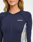 Billabong Womens Sunset Nomad Pipa Long Sleeve Sunshirt in Classic Navy close up view highlighting the recycled polyester stretch fabric texture secure full-zip front construction detailed printed sleeve panels quality stitching and signature Billabong branding, sold by Point Break Cambridge local family surf shop at 63 Duke Street.