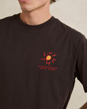 A close-up of a person wearing a dark brown t-shirt with a red graphic on the left chest. The graphic features a stylized sun and the text 'OFF THE WALL-WOARD FATH SOFTYTIME' and 'EST. Rhythm Mens Cactus SS T-Shirt - Vintage Black