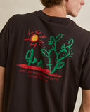 A close-up back view of a person wearing a dark brown t-shirt with a colorful graphic print of a cactus, sun, and the text 'OFF THE WELL-WORN PATH'. Rhythm Mens Cactus SS T-Shirt - Vintage Black
