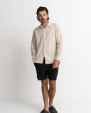 A man wearing a light beige long-sleeve linen button-up shirt and black shorts, standing against a plain white studio background. Rhythm Men's Classic Linen LS Shirt – Sand