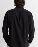 A man viewed from behind wearing a black long-sleeve button-up shirt, showing the back collar and shoulder details against a plain light gray background. Rhythm Men's Classic Linen LS Shirt – Vintage Black