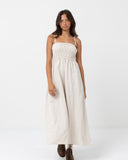 A woman modeling a cream-colored linen maxi dress with thin spaghetti straps and a smocked bodice, set against a plain white studio background. Rhythm Classic Shirred Midi Dress - Oat