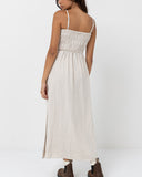 A woman modeling a light beige linen maxi dress with thin spaghetti straps and a smocked bodice, shown from the back against a plain white studio background. Rhythm Classic Shirred Midi Dress - Oat