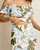 A woman wearing a two-piece tropical print set featuring a ruffled off-the-shoulder crop top and a matching high-waisted skirt. The floral pattern is in light blue, olive green, and taupe on an off-white background. Front view of the blue floral Rhythm Gigi Skirt showing the straight relaxed fit, mid-thigh length, and clean waistband design.