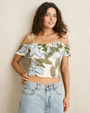 A woman modeling a cream off-the-shoulder crop top with a blue and green floral print, paired with light-wash denim jeans, against a plain beige wall. Front view of the blue floral Rhythm Gigi Top showing the square neckline and relaxed tank silhouette. 
