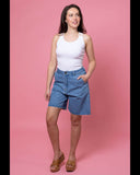 Woman wearing a white tank top and blue denim shorts on a pink background